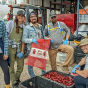 group of five people face the camera above red chiles at processing facility