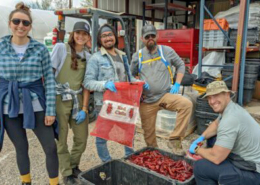 group of five people face the camera above red chiles at processing facility