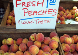 boxes of peaches at a farmers market with a sign reading Fresh Peaches