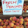 boxes of peaches at a farmers market with a sign reading Fresh Peaches