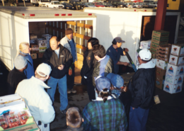 people conversing around a truck with boxes of produce