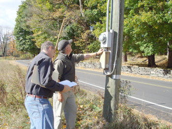 two men reading an electrical meter near a road