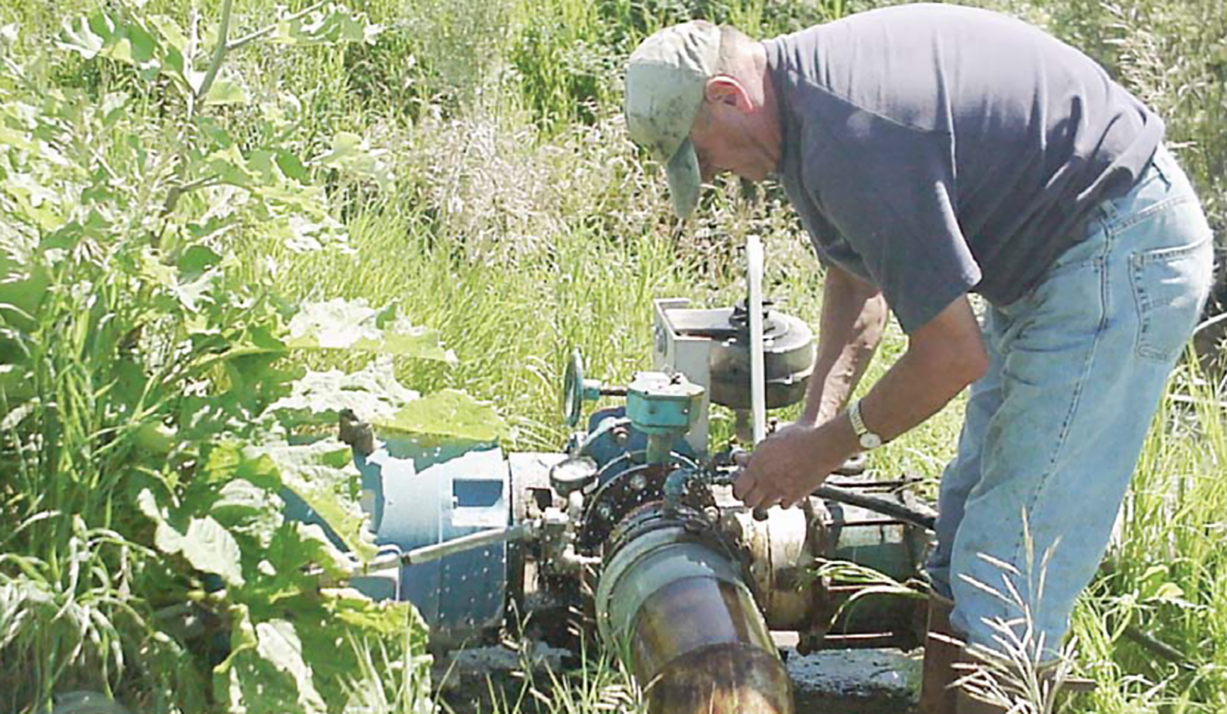 a man fixing a pump near a stream bank