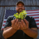 A veteran holding herbs, standing in front of American flag.