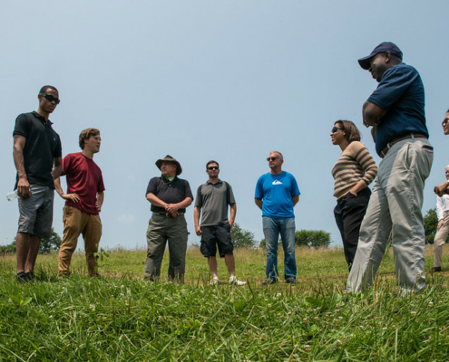 up-angle photo of group of people standing in an arc in a green field under blue sky.