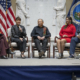 five people sit on chairs on a stage in front of U.S. and USDA flags