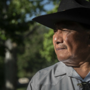 side-profile portrait of man in black hat , gray shirt, and inlaid bolo tie.