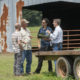 Four people standing and talking in front of an open barn door, with a trailer in the foreground