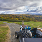 tractor in foreground with road into distance with forest with fall foliage and sky with clouds in background