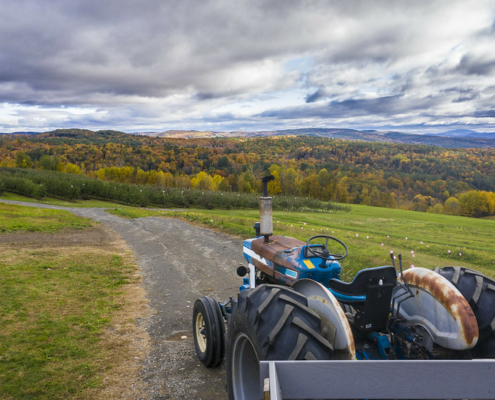 tractor in foreground with road into distance with forest with fall foliage and sky with clouds in background