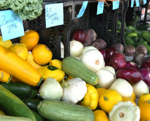 Vegetables (onions and squash) displayed at a farmers market with price signs