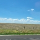 Fence crosses rangeland adjacent to a road with blue sky and white clouds above