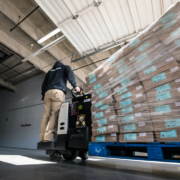 person riding on equipment transporting a pallet of boxes inside a building