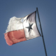 tattered Texas flag on a pole against blue sky, backlit