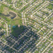 aerial photo showing streets, houses, and cloud shadows on a green landscape