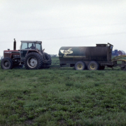 A tractor pulls a tank sprayer across a field, under cloudy sky.