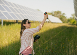 person standing in a field between solar panels, aiming a digital thermometer upward