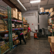 food boxes sit on shelves in a storage room, with two workers moving boxes