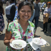 smiling person holding two bowls of ice cream within a crowd, outdoors