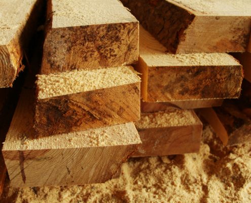 Stacked lumber with sawdust on the ground around it.