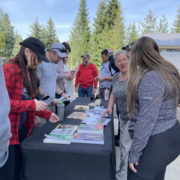 people stand outdoors around a table covered with books