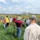 a group of people stand in a field under blue sky with clouds