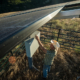 looking down on a person in a cowboy hat making adjustments to controls for a solar panel surrounded by fence.