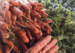 bundles of carrots with tops, tied with string, with loose Brussels sprouts behind