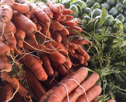 bundles of carrots with tops, tied with string, with loose Brussels sprouts behind