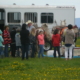 a group of children stand looking at saddled horses tied to a horsetrailer