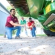 three people look at a rotating mill mounted on the bottom of a combine