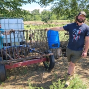 Two people stand outdoors with hands resting on a piece of farm equipment on wheels.