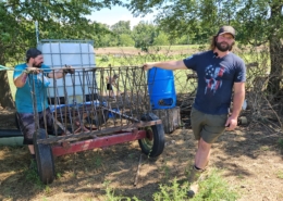 Two people stand outdoors with hands resting on a piece of farm equipment on wheels.