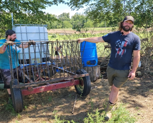 Two people stand outdoors with hands resting on a piece of farm equipment on wheels.