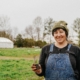 person in overalls, standing outdoors, holding plant seedling