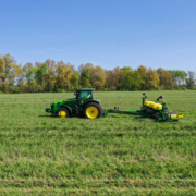 A tractor pulls seeding equipment across a green field under blue sky, with trees on horizon line