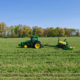 A tractor pulls seeding equipment across a green field under blue sky, with trees on horizon line