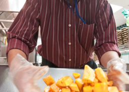 person stirs squash cubes with a gloved hand