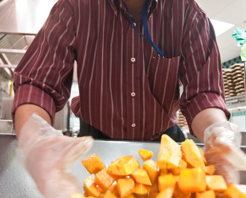 person stirs squash cubes with a gloved hand