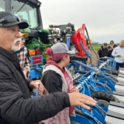 people gathered around a tractor with field equipment as a person explains