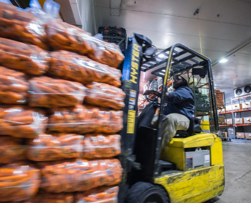 A forklift driver moves bags of carrots through a warehouse.