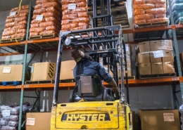 A forklift lifts bagged carrots onto shelves in a warehouse