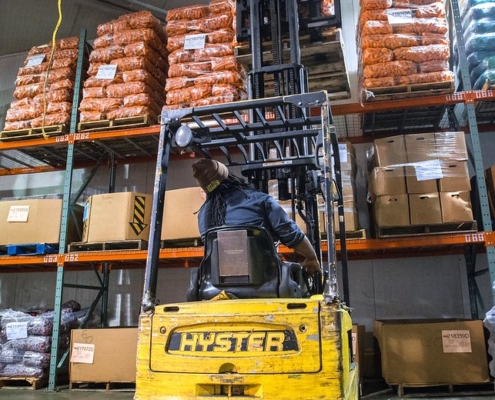 A forklift lifts bagged carrots onto shelves in a warehouse