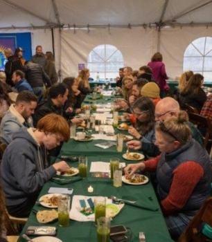 Participants in a farm-to-table dinner sit eating around a long table under a tent. 