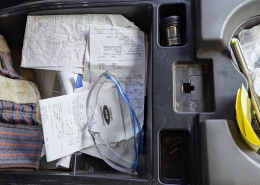 A pile of farm receipts sit in a truck console, along with safety glasses and work gloves.