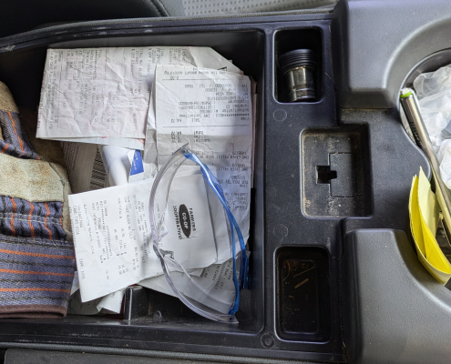 A pile of farm receipts sit in a truck console, along with safety glasses and work gloves.