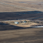 aerial view of farmstead buildings and trees surrounded by brown cultivated land