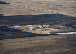 aerial view of farmstead buildings and trees surrounded by brown cultivated land