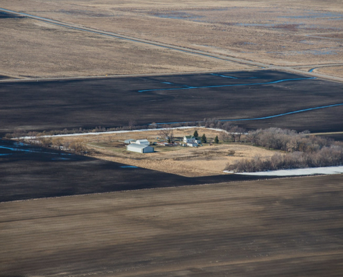 aerial view of farmstead buildings and trees surrounded by brown cultivated land