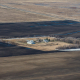 aerial view of farmstead buildings and trees surrounded by brown cultivated land